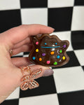 Hand holding a small chocolate teapot with colorful polka dots against a black and white checkered background.