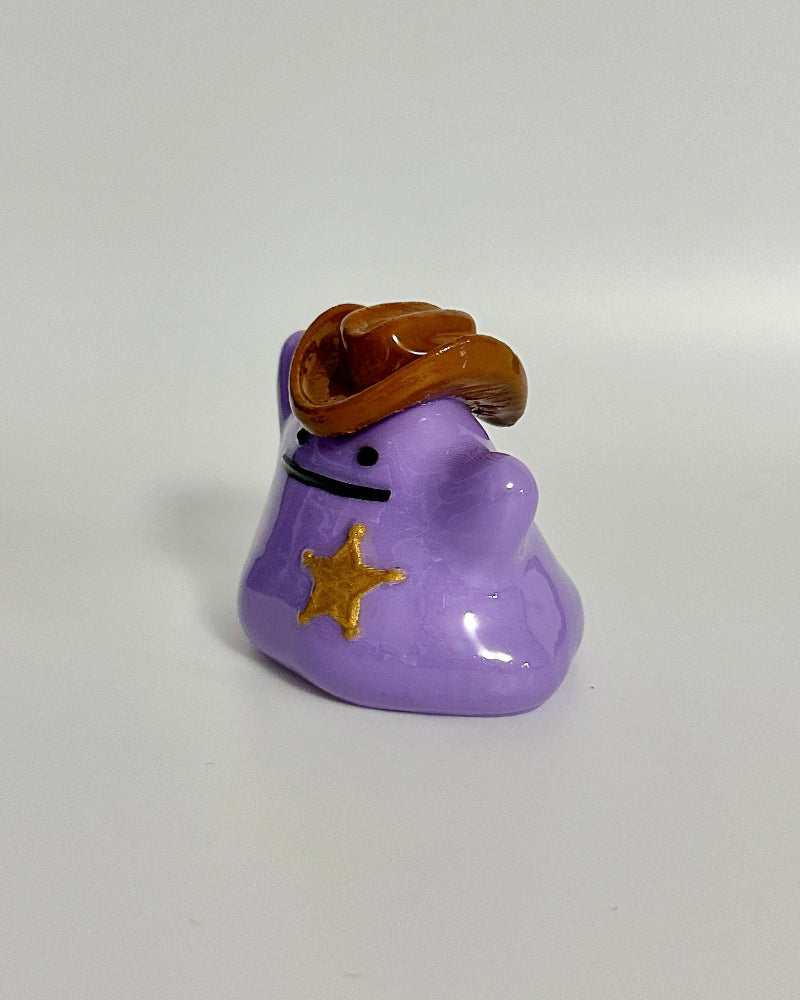 Small purple figurine with a brown hat and gold star on a white background