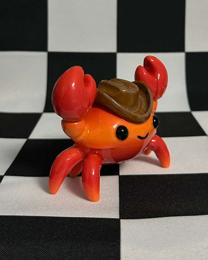 Small red crab figurine with a brown shell on a black and white checkered background