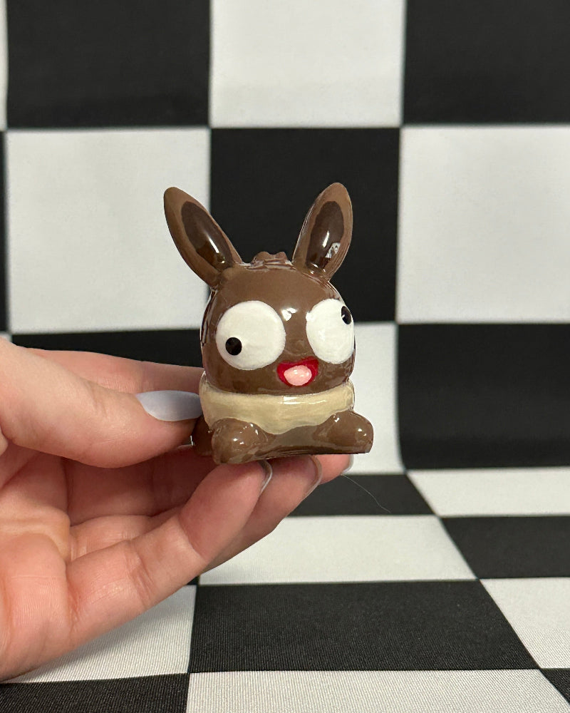 Hand holding a small chocolate bunny figurine against a black and white checkered background