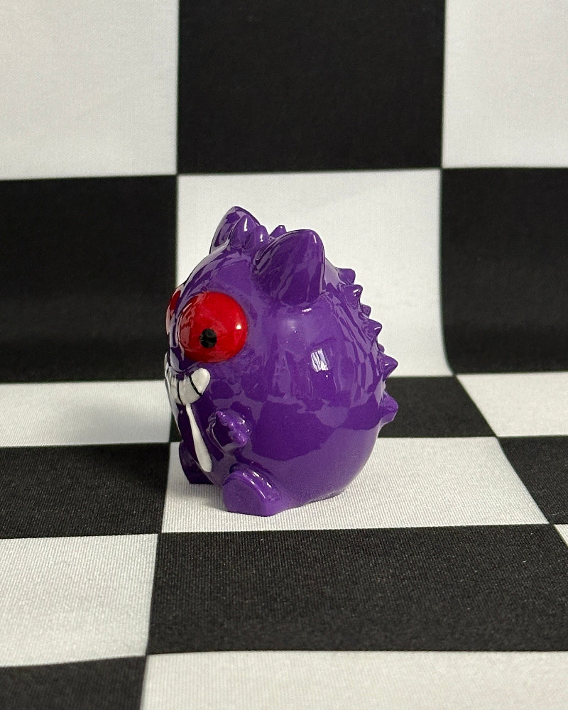 Purple toy figure with a red eye on a black and white checkered background