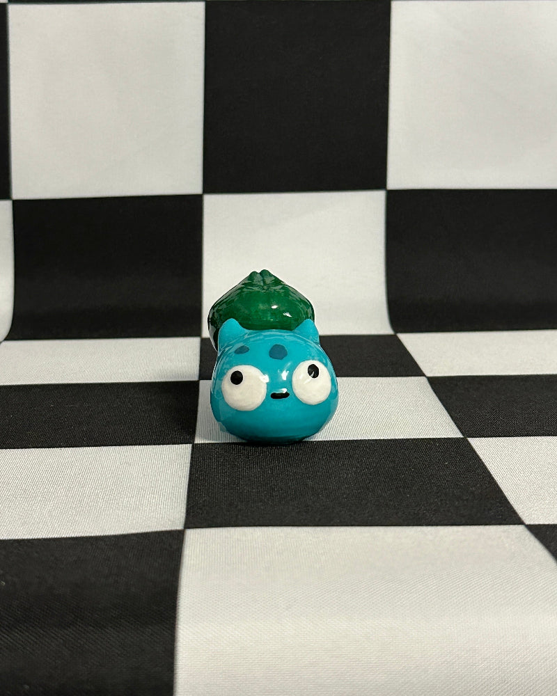 Small blue creature figurine with green hair on a black and white checkered background