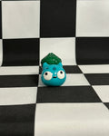 Small blue creature figurine with green hair on a black and white checkered background