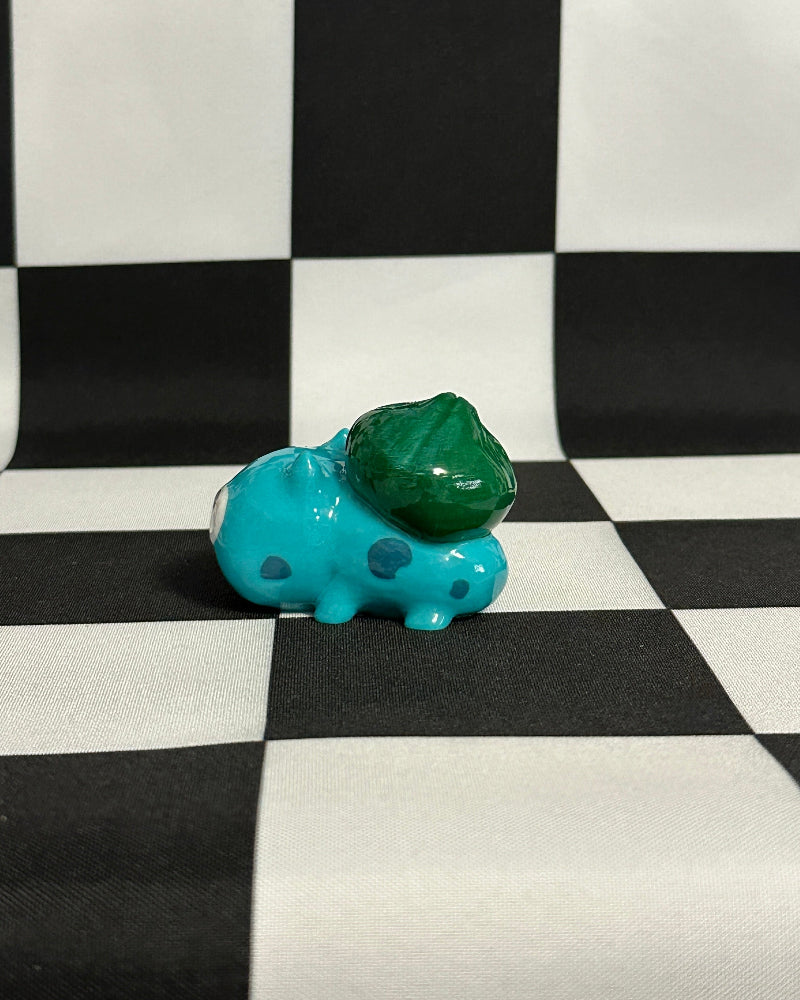 Small blue hippo figurine with a green object on a black and white checkered background