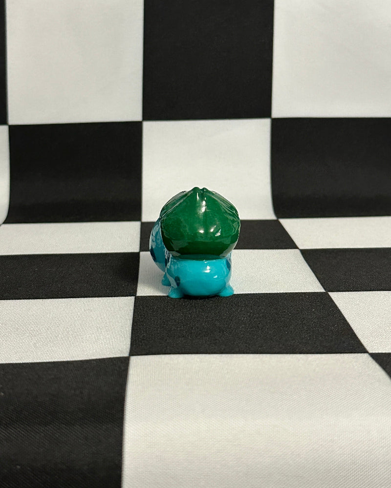 Small green and blue figurine on a black and white checkered background