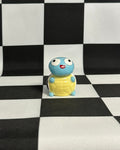 Small blue and yellow figurine on a black and white checkered background