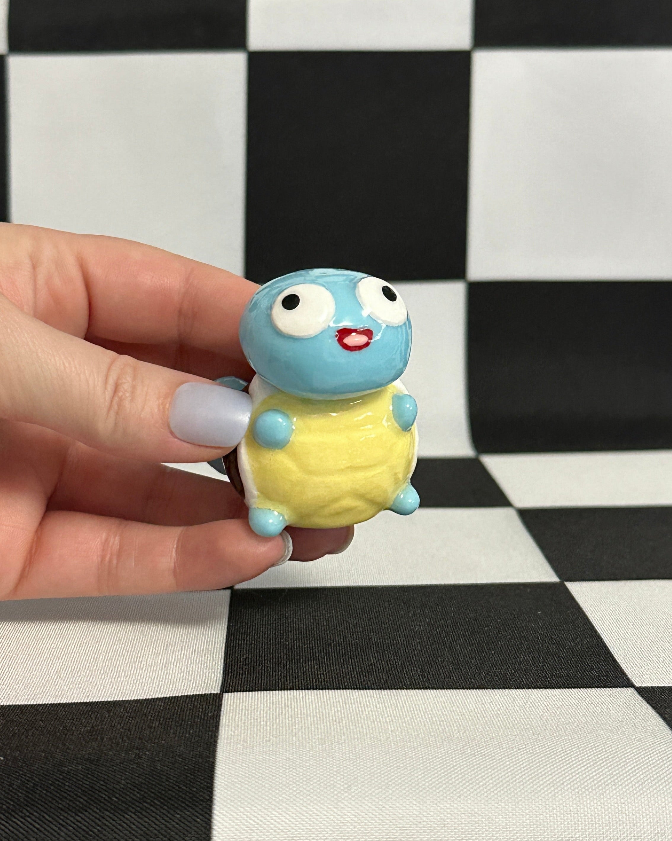 Small blue and yellow figurine held in a hand against a black and white checkered background