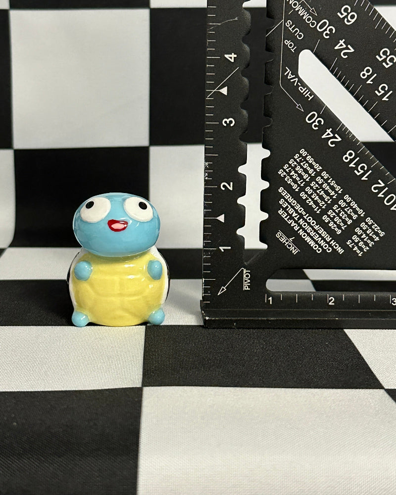 Small turtle figurine next to a ruler on a checkered background