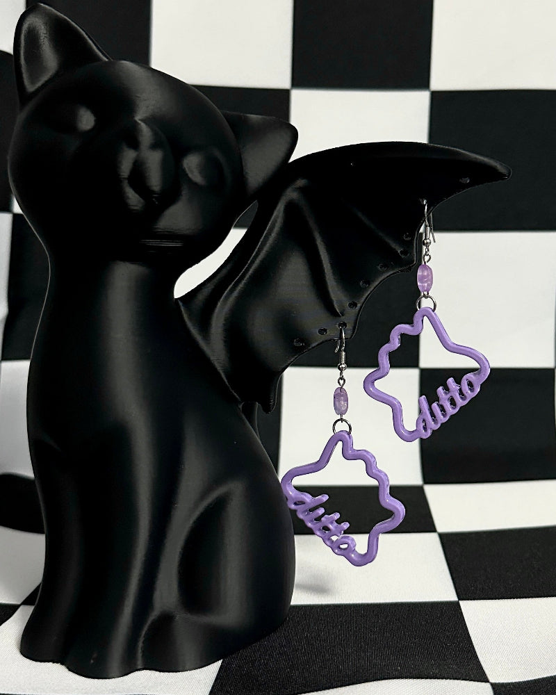 Black cat figurine with purple 'kitten' earrings on a black and white checkered background