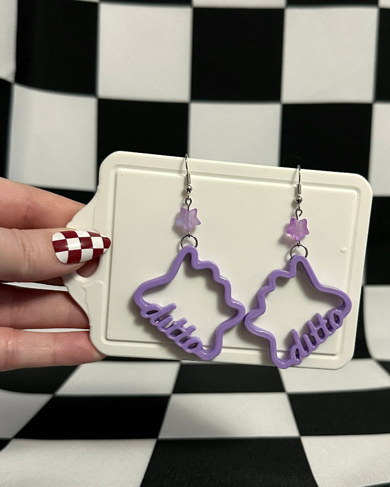 Purple earrings on a white card held by a hand against a black and white checkered background