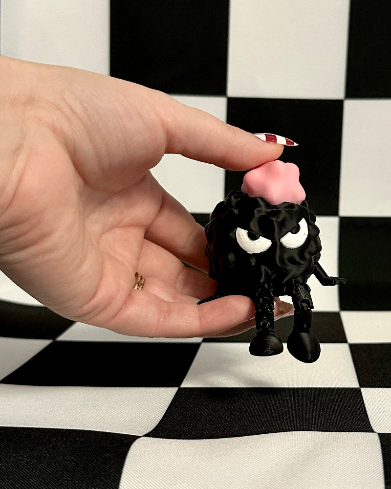 Hand holding a small black cat figurine with pink bow on a checkered background