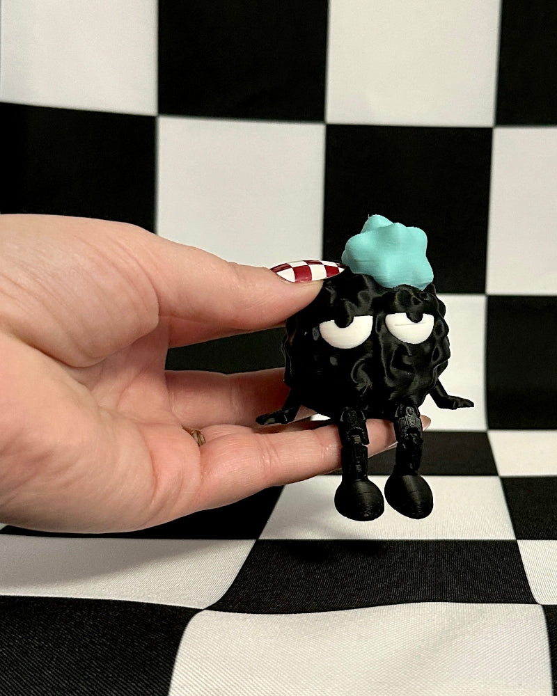 Small black creature with a blue head held in front of a checkered background