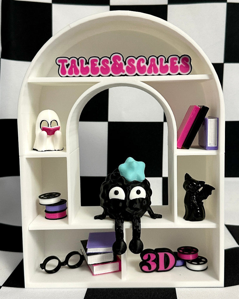 White arch-shaped display shelf with toys and 'Tales & Scapes' branding on a black and white checkered background.
