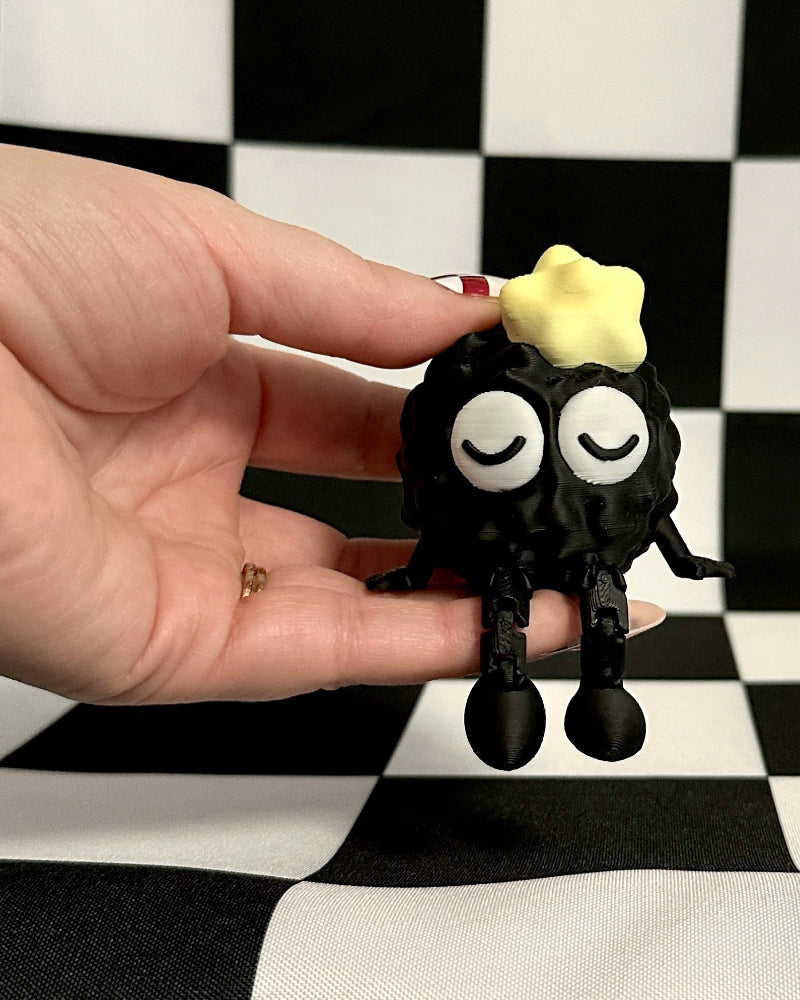 Hand holding a small black figurine with a yellow star on a checkered background