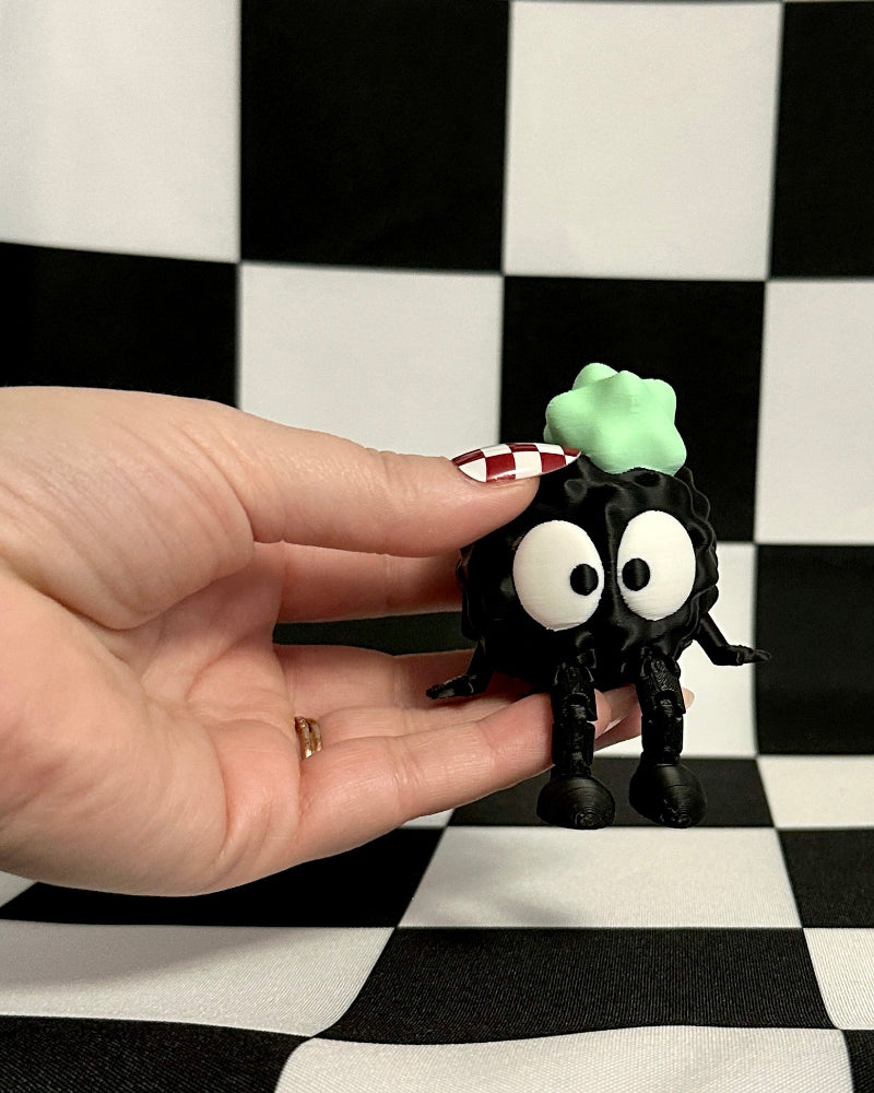 Small black figurine with a green object on a checkered background