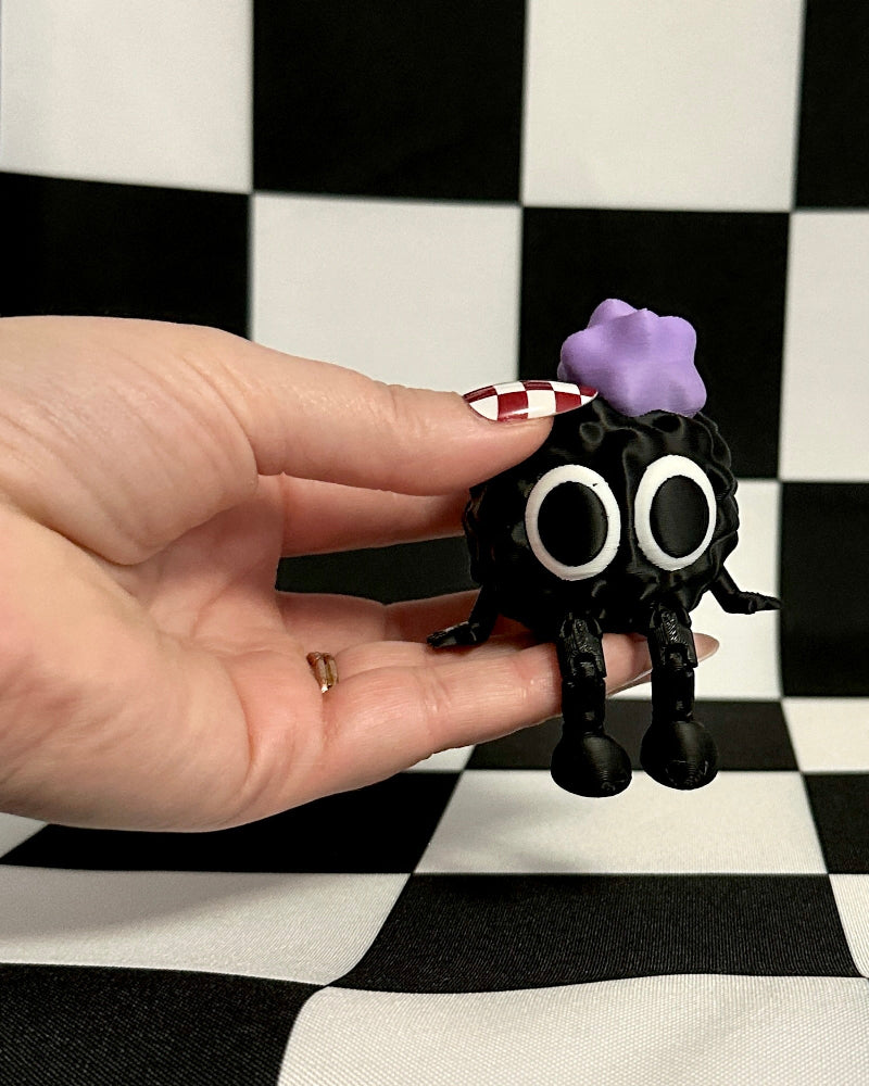 Small black figurine with a purple object on a checkered background