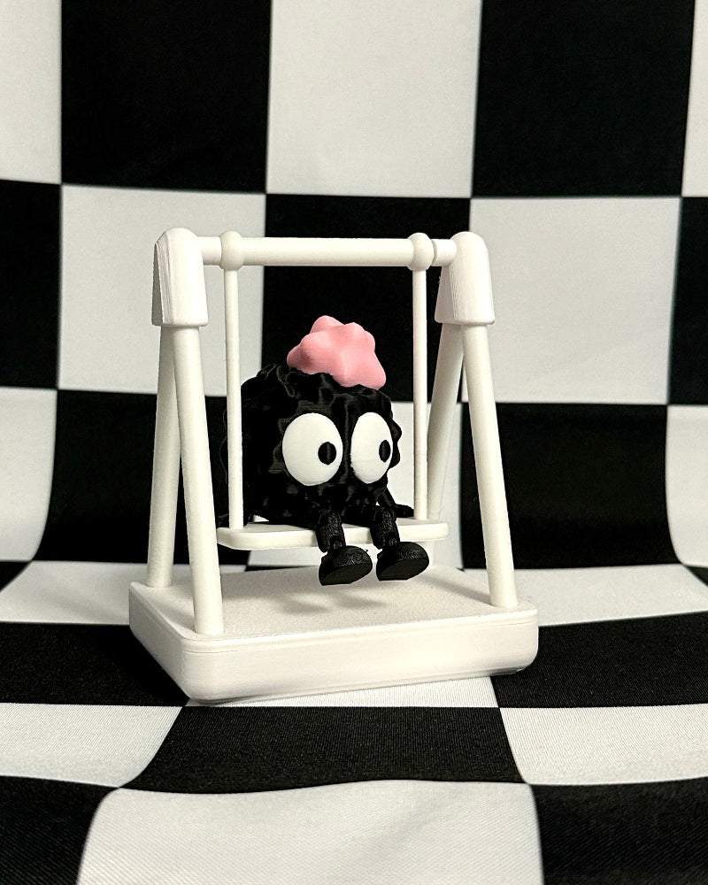 Small figurine of a character with a pink head on a white swing against a black and white checkered background