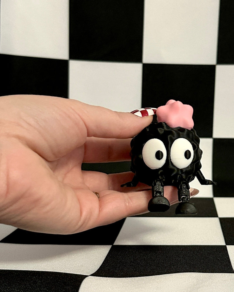 Hand holding a small black and pink toy figure against a checkered background