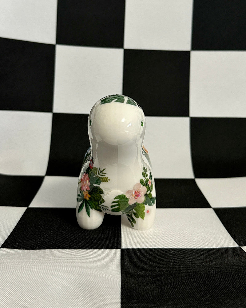 Small white ceramic dog figurine with floral design on a black and white checkered background