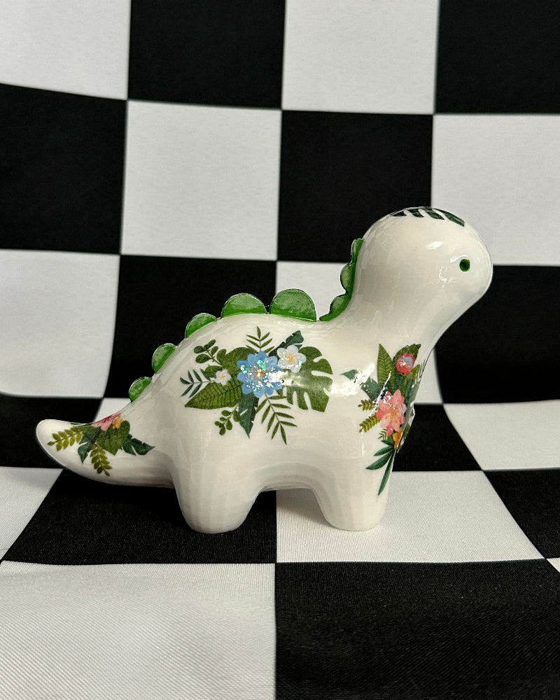 Decorative ceramic dinosaur figurine with floral patterns on a black and white checkered background