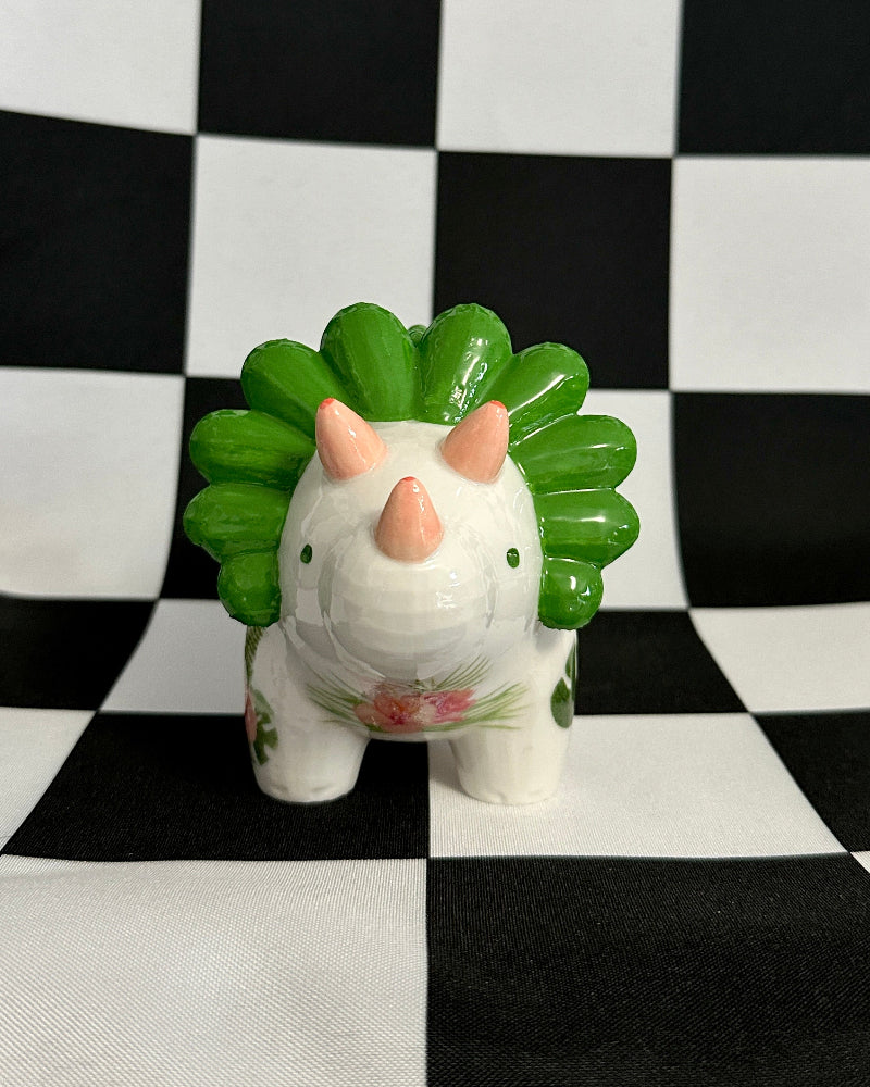 Small ceramic animal figurine with green leaf-like top on a black and white checkered background