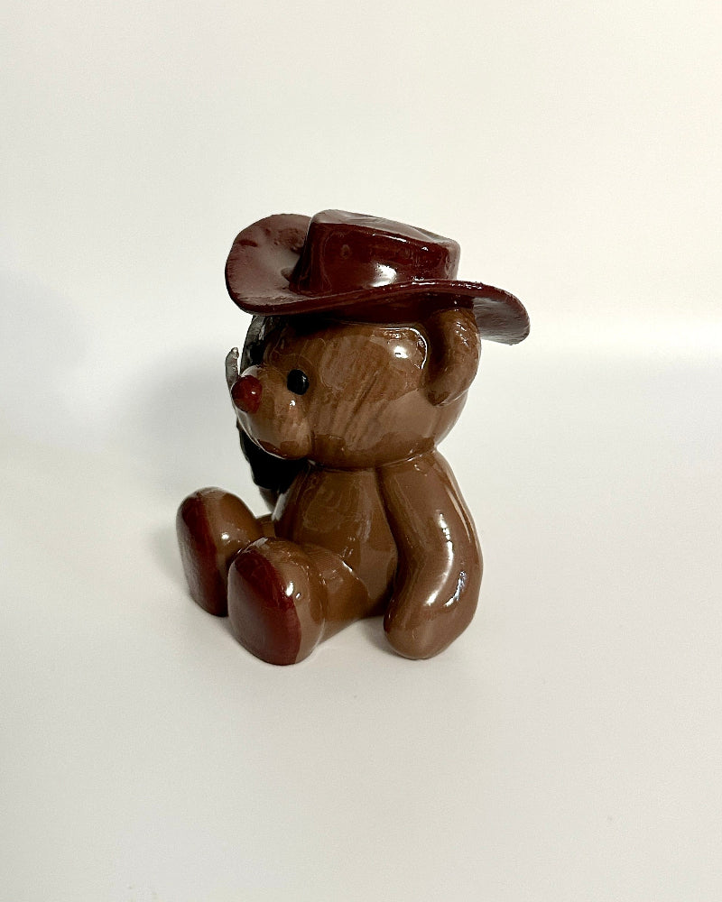 Small brown teddy bear figurine wearing a hat on a white background