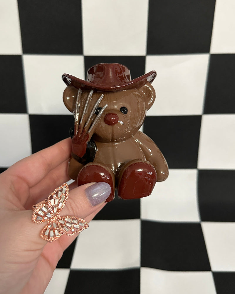 Small brown teddy bear with a cowboy hat held against a black and white checkered background.