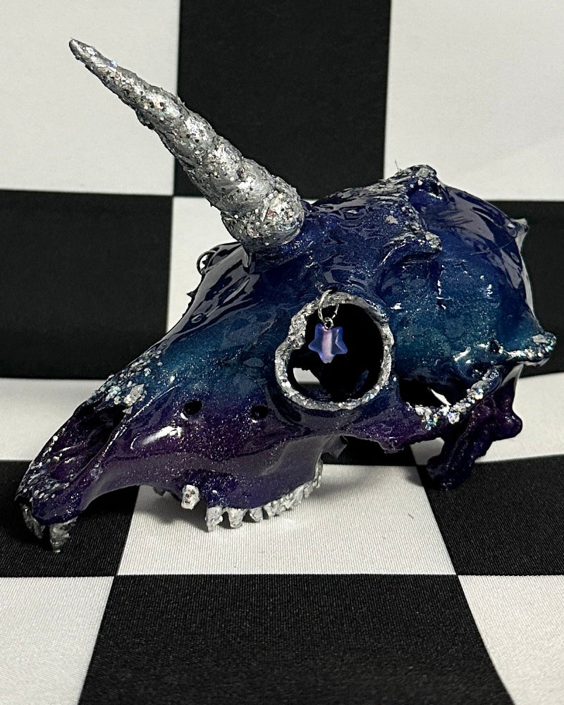 Blue unicorn skull with silver horn on a black and white checkered background