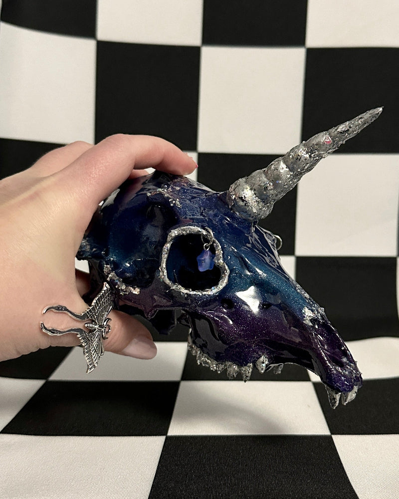 Hand holding a decorative unicorn skull against a black and white checkered background