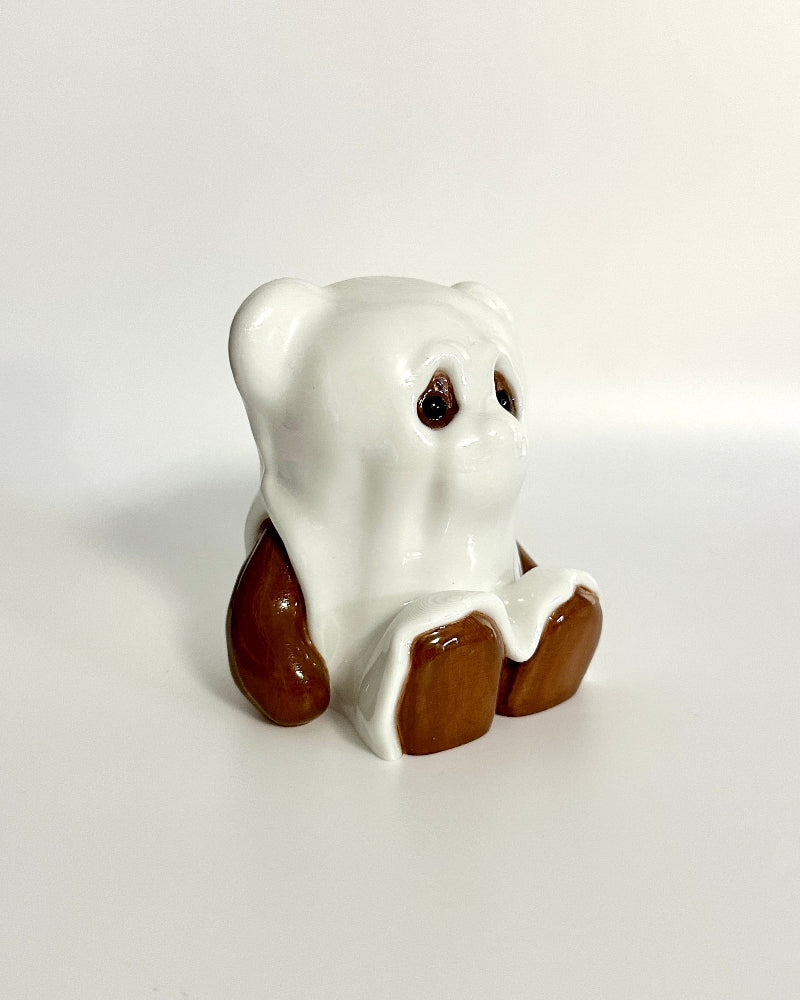 Small white ghost figurine with brown shoes on a light gray background