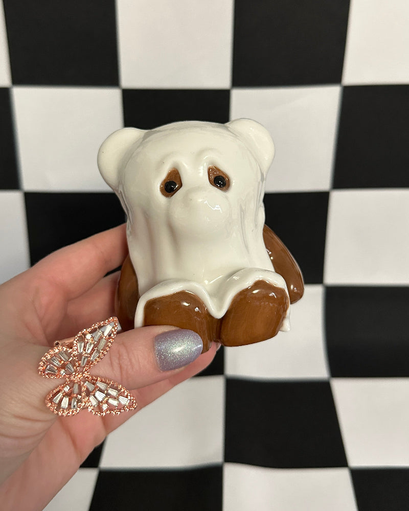 Hand holding a small bear-shaped cookie against a checkered background