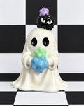 A ceramic ghost figurine holding a blue and green star, with a small black creature on its head and a purple flower crown, set against a black and white checkered background.