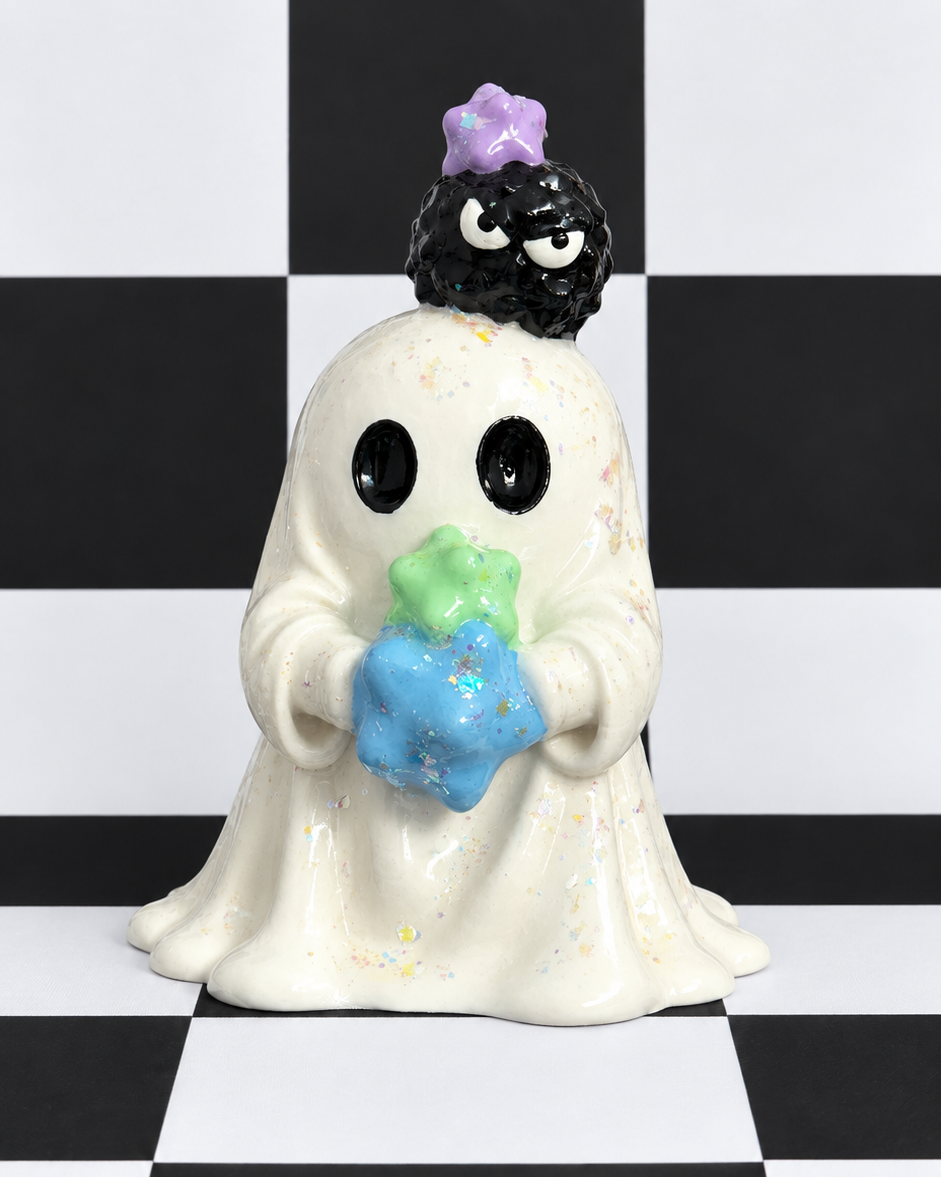 A ceramic ghost figurine holding a blue and green star, with a small black creature on its head and a purple flower crown, set against a black and white checkered background.