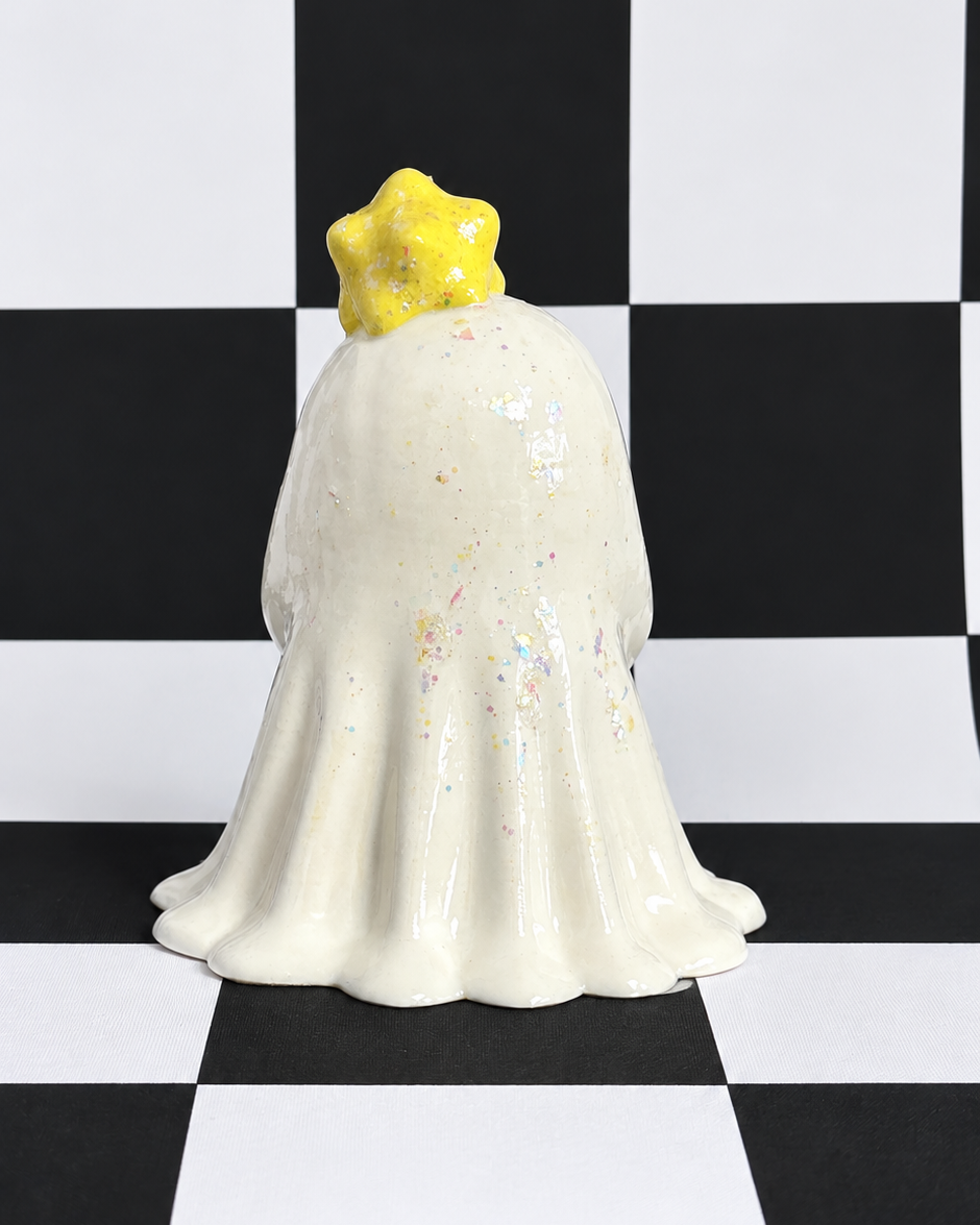 A ceramic ghost figurine with a yellow glittery star crown, standing on a black and white checkered background.