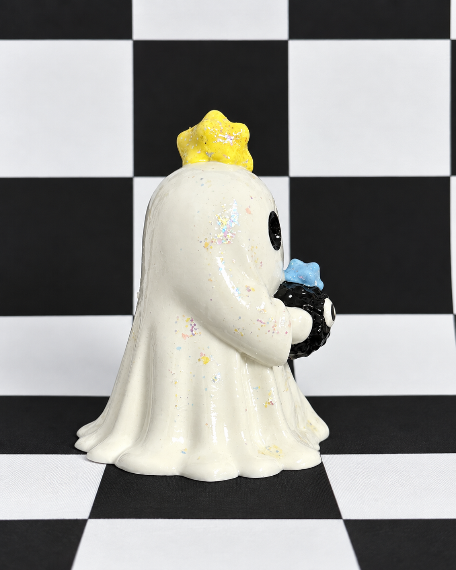 A glossy white ghost figurine with a yellow glitter crown, holding a black and blue skull, set against a black and white checkered background.
