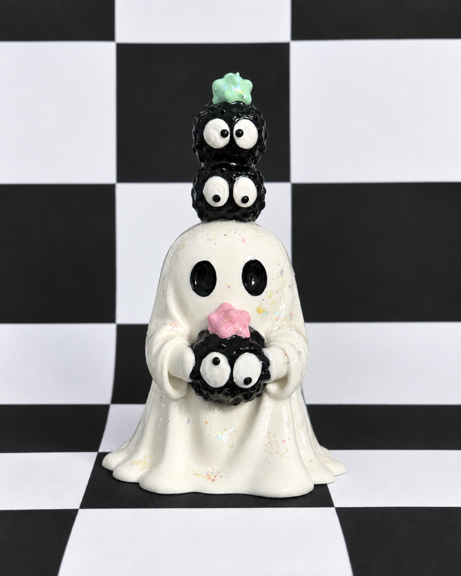 A ceramic ghost figurine with three stacked black cupcake toppers featuring white eyes, set against a black and white checkered background.