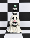 A ceramic ghost figurine with three stacked black cupcake toppers featuring white eyes, set against a black and white checkered background.