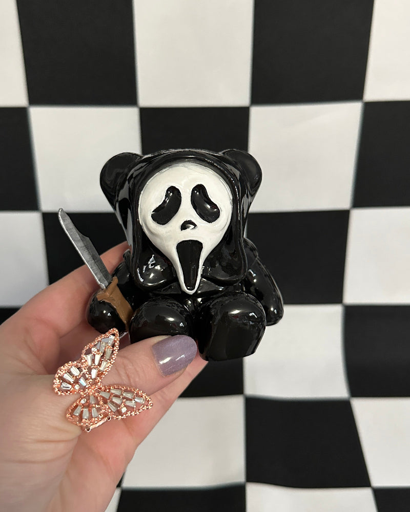 Black bear figurine with a white face holding a knife, held by a hand against a black and white checkered background.