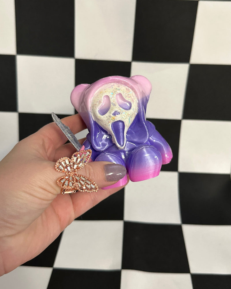 Hand holding a purple and pink hair tie with a ghost design against a checkered background