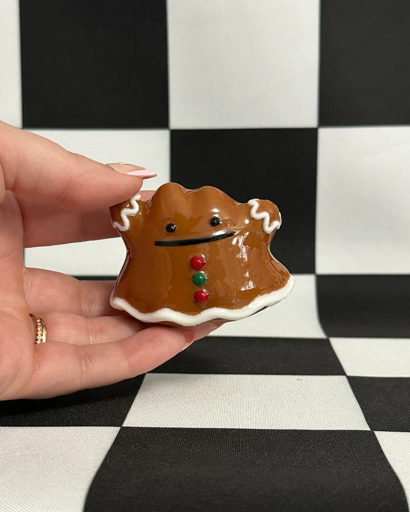 Hand holding a gingerbread cookie with a face on a black and white checkered background