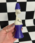Hand holding a small figurine with a blue top and white body against a black and white checkered background