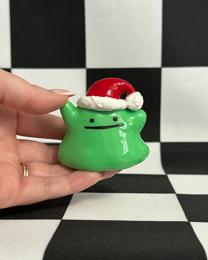 Green ghost with a Santa hat held by a hand on a checkered background