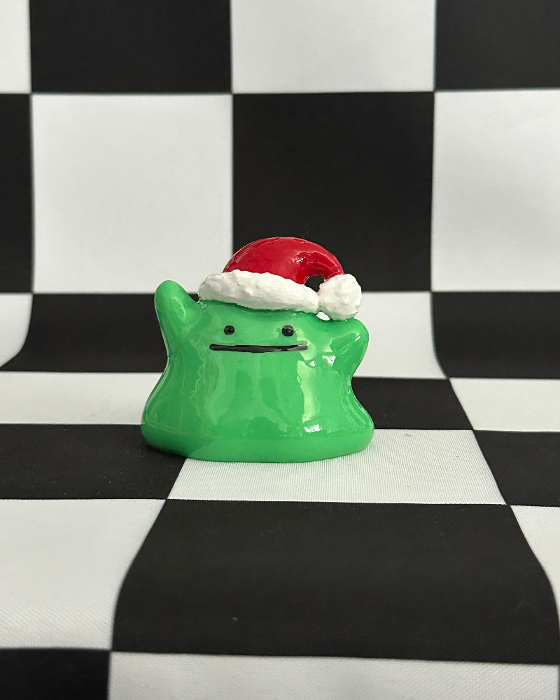 Green ghost figurine with a Santa hat on a black and white checkered background