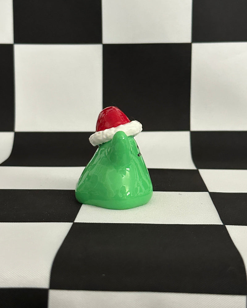 Green Christmas tree figurine with a red and white Santa hat on a black and white checkered background