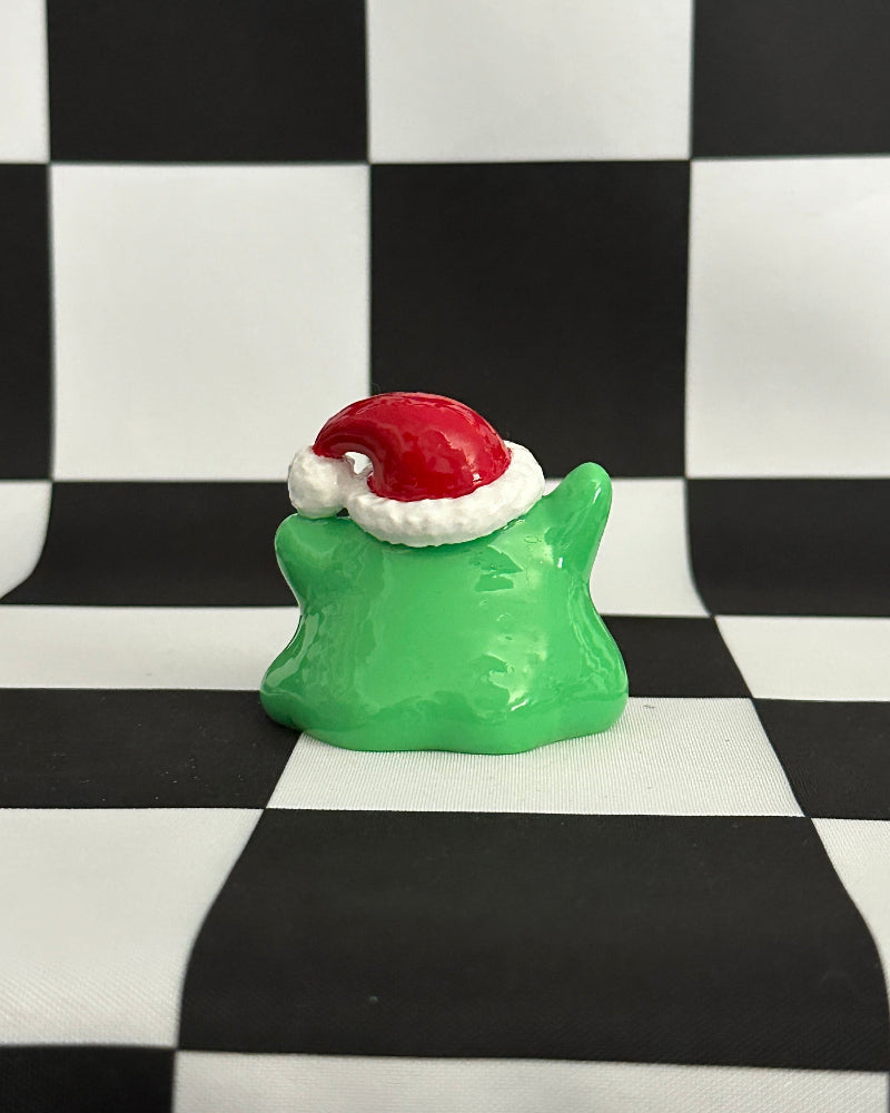 Green star-shaped object with a red and white Santa hat on a black and white checkered background