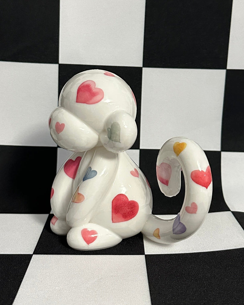 Small figurine of a white cat with red hearts on a black and white checkered background
