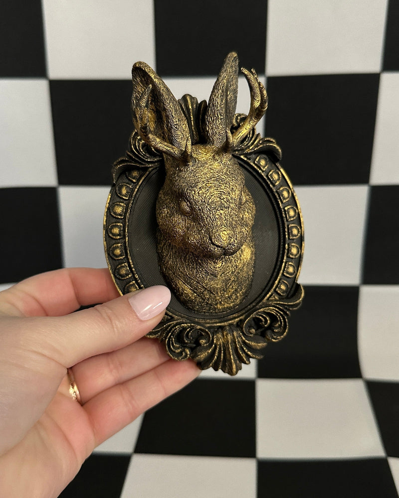 Decorative rabbit head sculpture in a decorative frame held against a black and white checkered background.