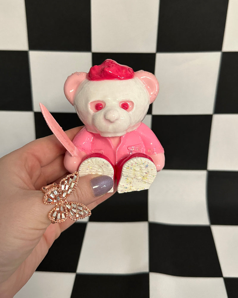 Small pink and white bear figurine held in a hand against a black and white checkered background
