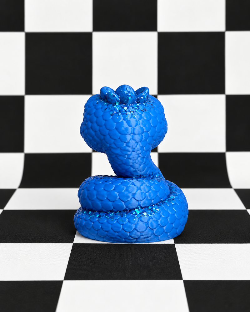 A bright blue coiled snake figurine with a textured, glittery scale pattern, set against a black and white checkered background.