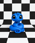 A bright blue coiled snake figurine with large glossy black eyes, centered on a black-and-white checkered surface and backdrop.